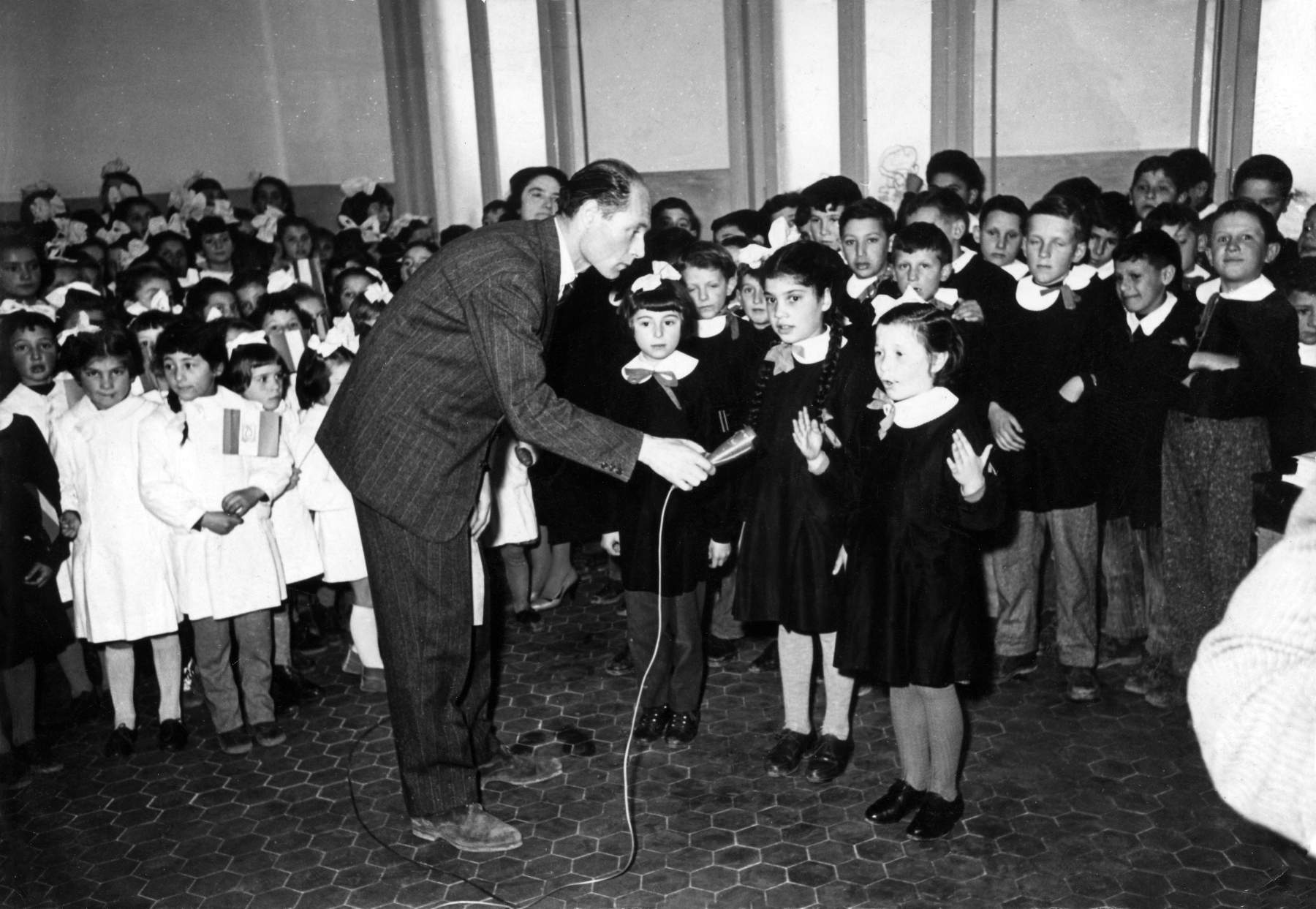 Recita scolastica in occasione della visita del direttore scolastico anno 1956. Stanno recitando da sx: Lucia Gherlenda, Annamaria Forcellini, Fiorenza Bianchin. Bambine col grembiule bianco classe 1950, Maria Teresa Morellato, Lucia Forcellini, Giuliana Cimenti e altre, dietro al direttore si intravede la maestra Baron.